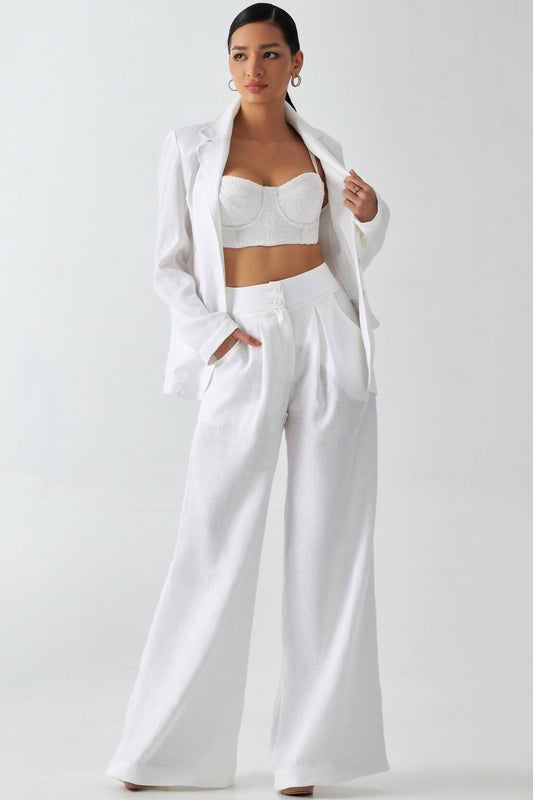 A model wearing a white linen blazer with a left front pocket, side pockets, and a 3 button single breasted front closure.